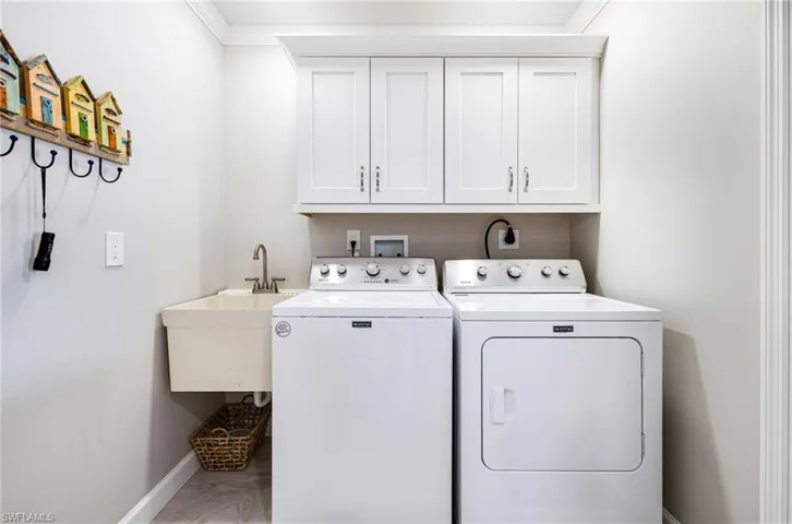 Laundry room featuring cabinets, sink, crown molding, and washing machine and clothes dryer