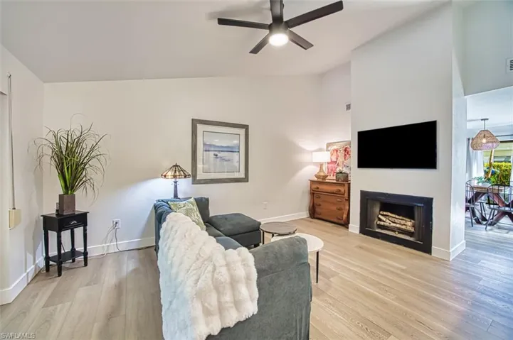 Living area with vaulted ceiling, a ceiling fan, light wood-type flooring, a fireplace, and baseboards