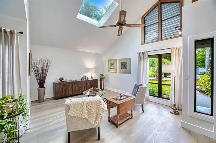Living area featuring high vaulted ceiling, a ceiling fan, light wood-type flooring, a skylight, and baseboards