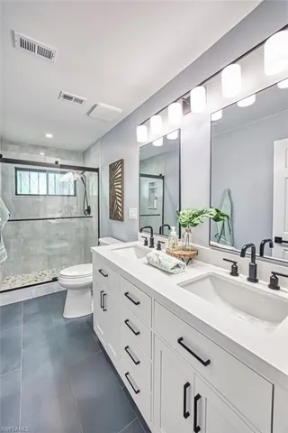 Full bathroom featuring double vanity, a stall shower, toilet, and tile patterned flooring