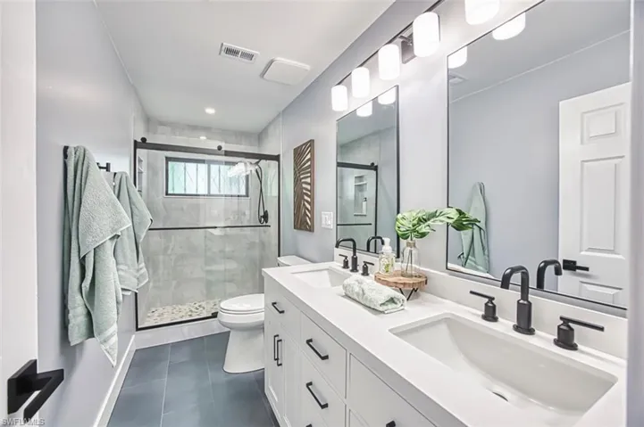 Full bath with toilet, tile patterned floors, double vanity, and a stall shower