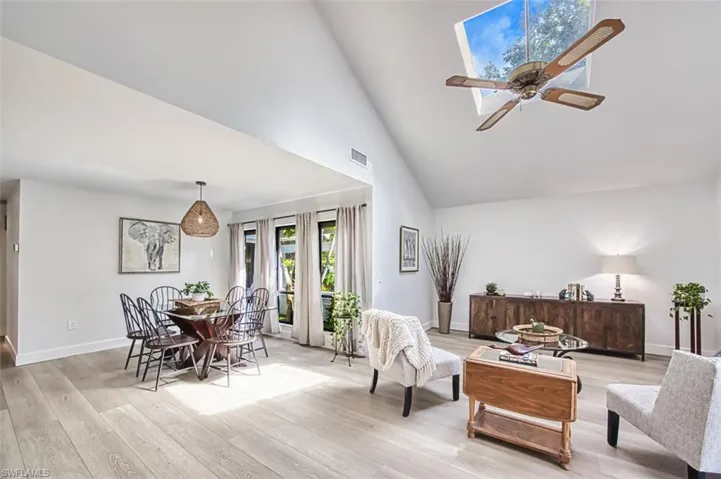 Living room featuring light wood-style flooring, high vaulted ceiling, a ceiling fan, and baseboards