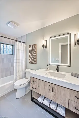 Bathroom with toilet, vanity, tile patterned flooring, and shower / bathtub combination with curtain