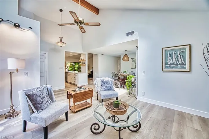 Living area with a ceiling fan, light wood-type flooring, baseboards, beamed ceiling, and high vaulted ceiling