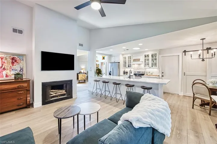 Living room with ceiling fan, a fireplace, a barn door, light wood finished floors, and high vaulted ceiling