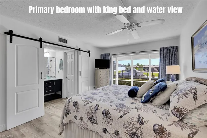 Primary bedroom with king bed has wonderful view through disappearing sliders. Vanity in ensuite bathroom is a recent update, along with the barn doors. Walk in closet is behind the closed door.