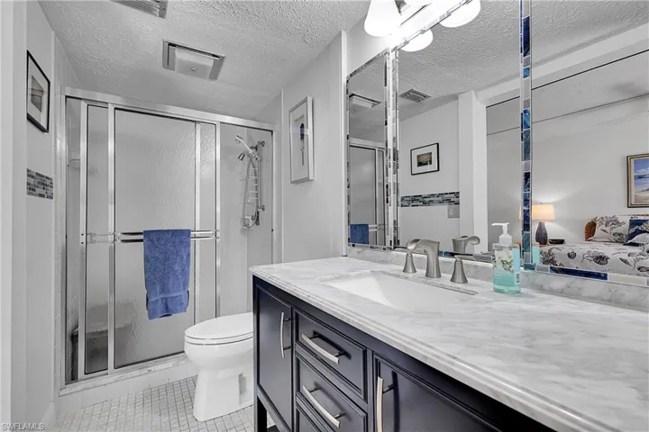 Ensuite primary bathroom with tiled step-in shower has updated vanity, toilet, and tile trim around the large mirror which hides medicine cabinets. Lots of storage!