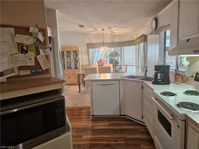 Kitchen featuring sink, white cabinetry, hanging light fixtures, a wealth of natural light, and white appliances