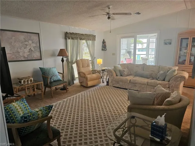 Carpeted living room featuring ceiling fan, lofted ceiling, and a textured ceiling