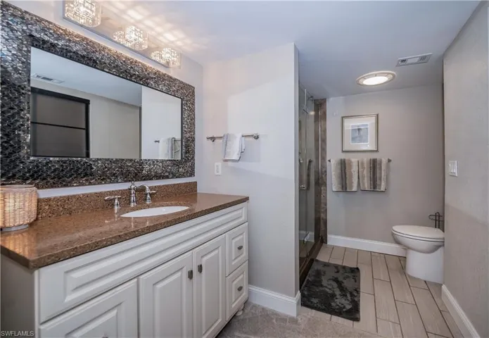 Bathroom with vanity, an inviting chandelier, a shower with shower door, and toilet