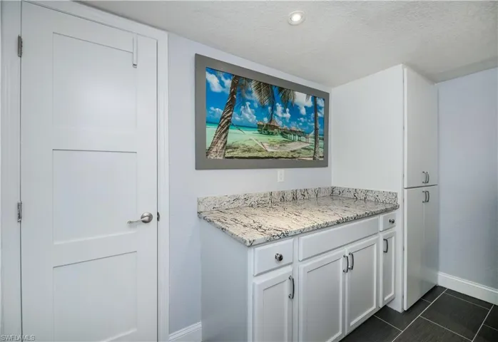 Bar with white cabinets, a textured ceiling, dark tile patterned floors, and light stone countertops