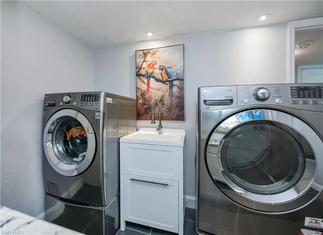 Clothes washing area with sink, dark tile patterned floors, separate washer and dryer, and cabinets