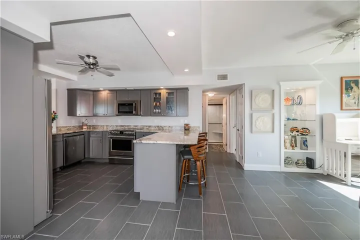 Kitchen featuring stainless steel appliances, ceiling fan, light stone countertops, and a breakfast bar