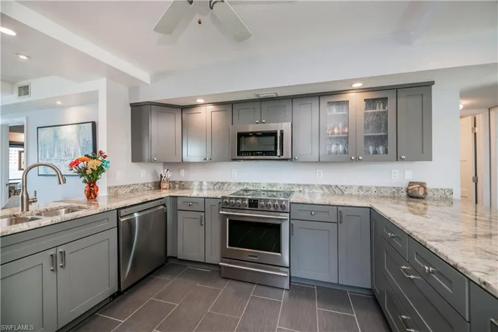 Kitchen with light stone counters, kitchen peninsula, stainless steel appliances, gray cabinets, and sink