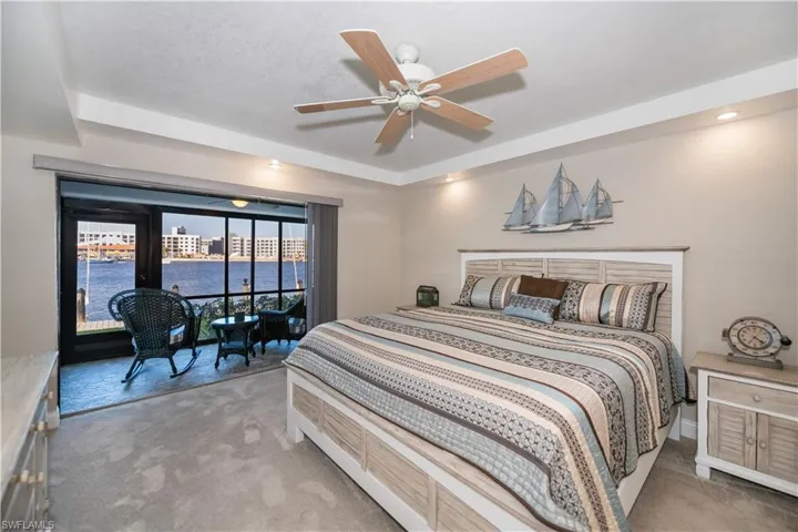 Bedroom with a raised ceiling, ceiling fan, light carpet, and a water view