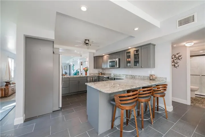 Kitchen featuring stainless steel appliances, ceiling fan, kitchen peninsula, a breakfast bar area, and gray cabinets
