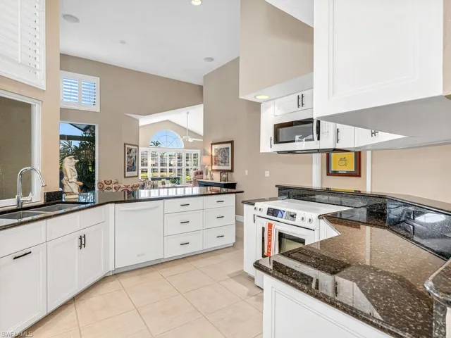 Kitchen featuring sink, white appliances, light tile patterned floors, dark stone countertops, and white cabinetry