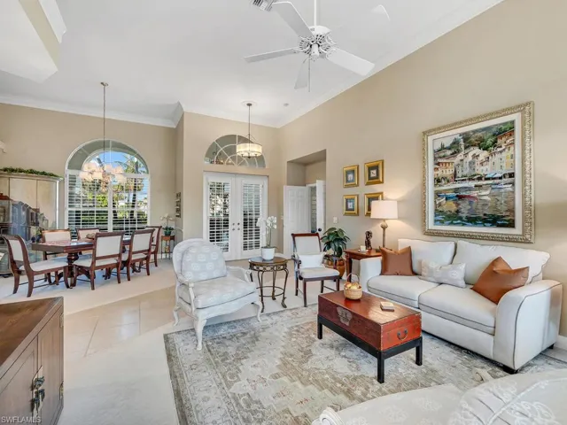 Tiled living room featuring a high ceiling, crown molding, ceiling fan with notable chandelier, and french doors