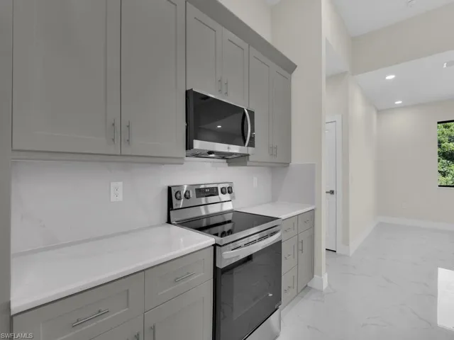Kitchen featuring appliances with stainless steel finishes, gray cabinets, light marble finish floors, and recessed lighting