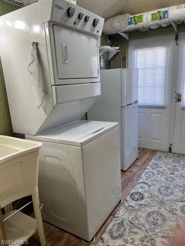 Laundry area with stacked washer and dryer and dark wood-type flooring