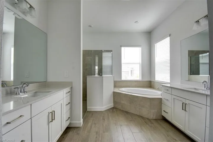 Full bathroom featuring two vanities, a bath, walk in shower, and light wood-type flooring