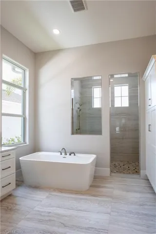 Full bath featuring a walk in shower, a freestanding bath, and recessed lighting