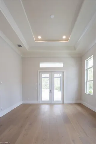 Spare room with light wood-type flooring, french doors, recessed lighting, crown molding, and a tray ceiling