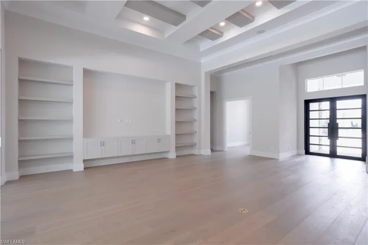 Unfurnished living room with built in features, french doors, a high ceiling, beam ceiling, and light wood finished floors