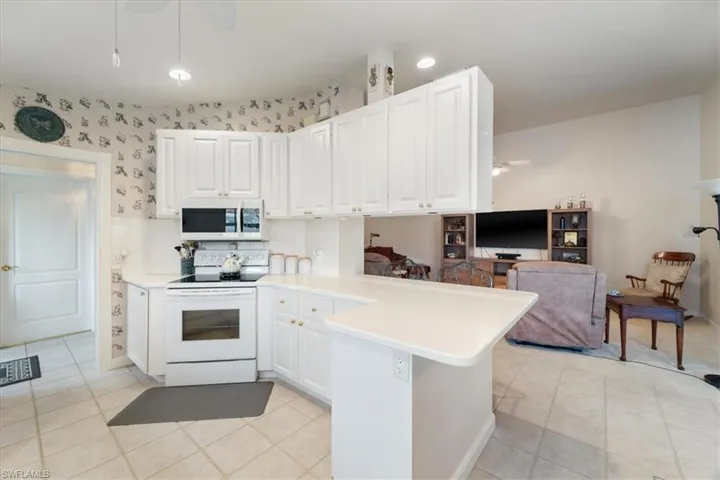 Kitchen with white appliances, ceiling fan, a peninsula, light countertops, and white cabinets
