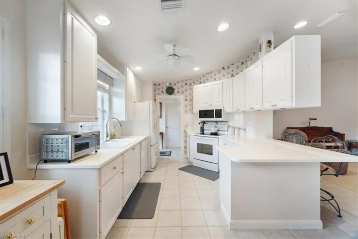Kitchen with light countertops, white appliances, a kitchen bar, white cabinetry, and light tile patterned floors