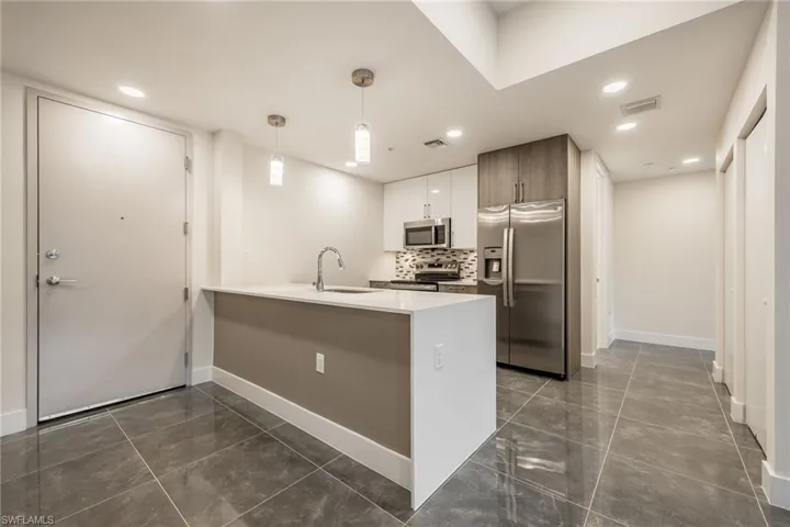 Kitchen with visible vents, a peninsula, stainless steel appliances, a sink, and backsplash