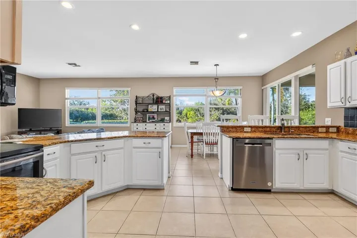 Kitchen featuring a peninsula, white cabinets, dark stone countertops, stainless steel appliances, and hanging light fixtures
