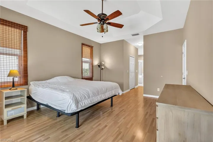 Bedroom featuring a closet, a raised ceiling, light wood finished floors, ceiling fan, and ensuite bath