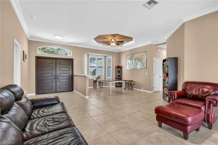 Living room with crown molding, a ceiling fan, light tile patterned floors, and a tray ceiling