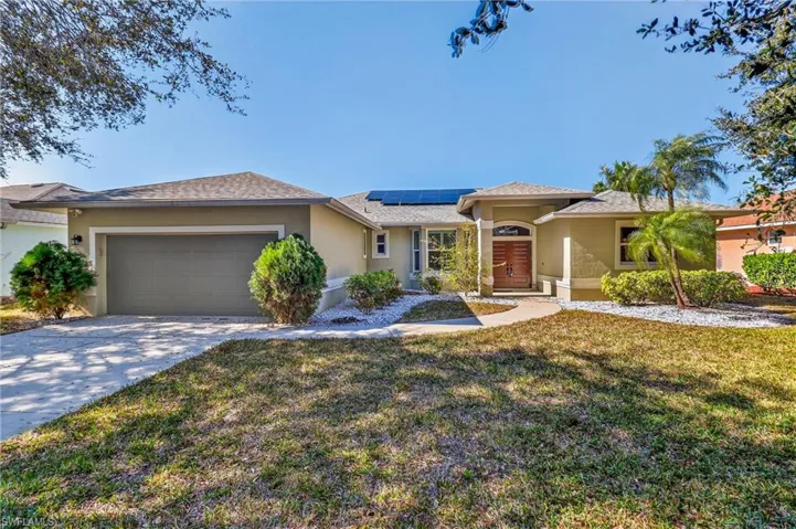 View of front of house with roof mounted solar panels, stucco siding, an attached garage, a front lawn, and driveway