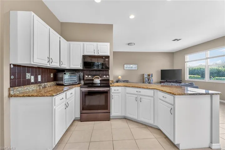 Kitchen with dark stone counters, stainless steel range with electric stovetop, a peninsula, decorative backsplash, and light tile patterned floors