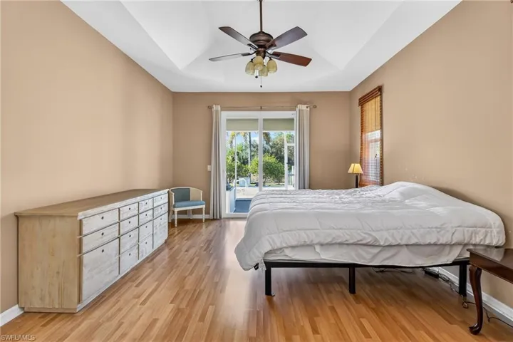 Bedroom with a tray ceiling, access to exterior, light wood-type flooring, and a ceiling fan