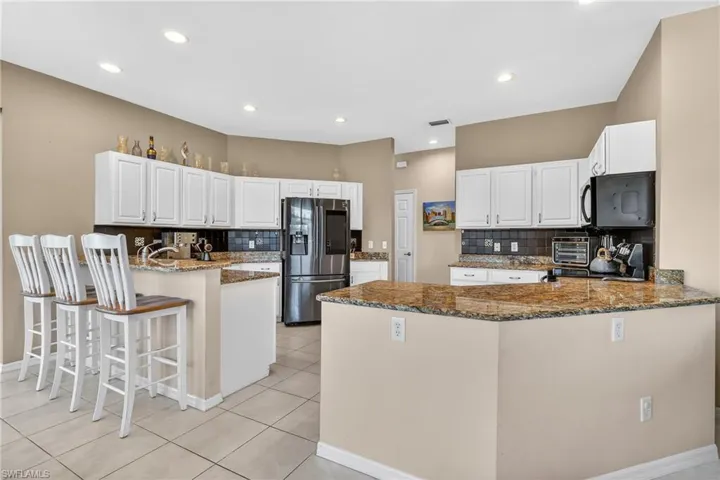 Kitchen with a peninsula, decorative backsplash, a kitchen bar, dark stone counters, and black appliances