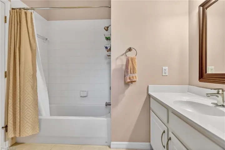 Bathroom with vanity, shower / bathtub combination with curtain, and light tile patterned floors