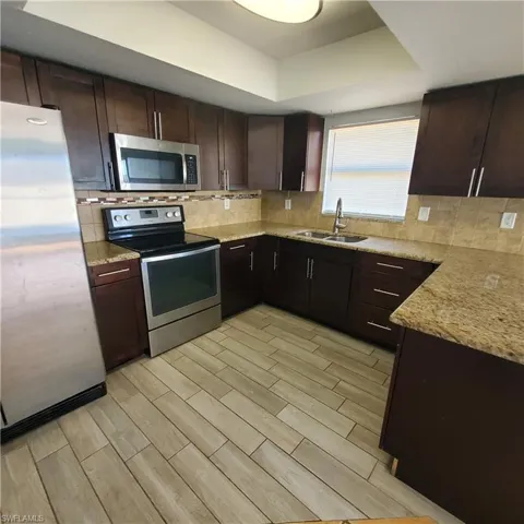 Kitchen with dark brown cabinets, stainless steel appliances, wood finish floors, light stone countertops, and tasteful backsplash