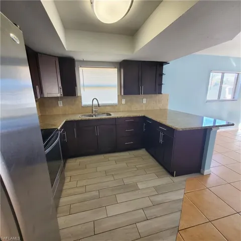 Kitchen featuring tasteful backsplash, freestanding refrigerator, light stone countertops, electric stove, and a peninsula