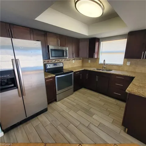 Kitchen featuring appliances with stainless steel finishes, dark brown cabinets, wood tiled floors, light stone counters, and a raised ceiling