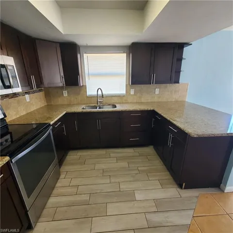 Kitchen featuring appliances with stainless steel finishes, wood finish floors, light stone countertops, and dark brown cabinetry