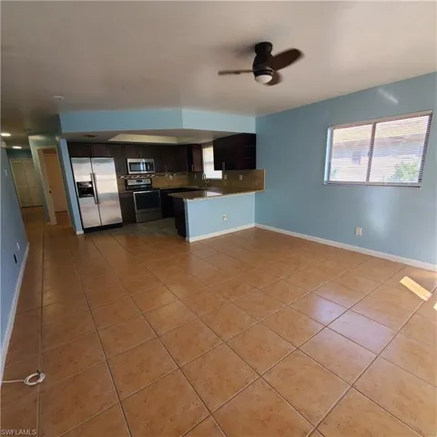 Kitchen featuring stainless steel appliances, open floor plan, light tile patterned flooring, dark brown cabinets, and a ceiling fan