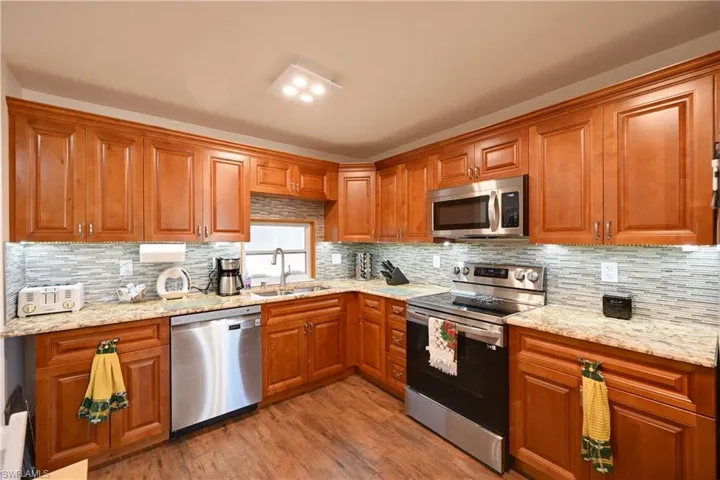 Kitchen featuring appliances with stainless steel finishes, brown cabinetry, and light stone countertops