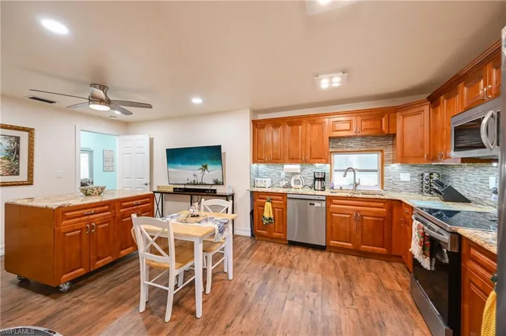 Kitchen with brown cabinetry, stainless steel appliances, light stone countertops, decorative backsplash, and recessed lighting