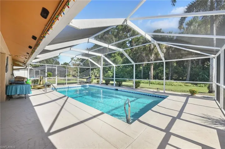 Outdoor pool with a sunroom, a patio, a lanai, and view of wooded area