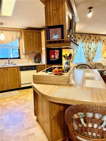 Kitchen with a textured ceiling, light countertops, white dishwasher, wood finish cabinetry, and decorative light fixtures