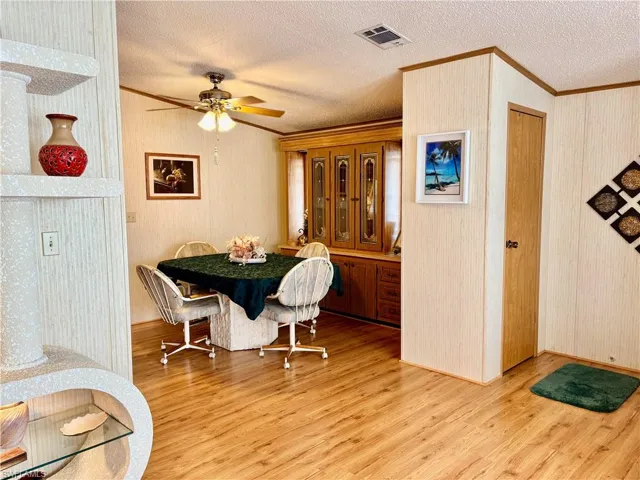 Dining area with crown molding, light wood-style flooring, a textured ceiling, and a ceiling fan