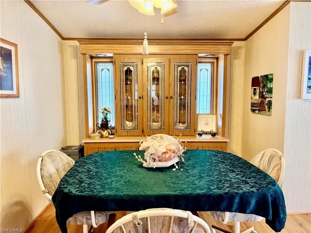 Dining area with crown molding, wood finished floors, a ceiling fan, a textured ceiling, and wallpapered walls